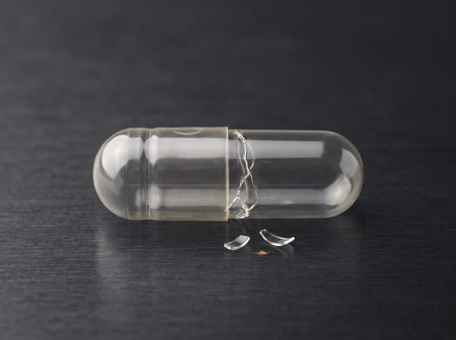 A clear capsule with a crack around its body and small shell fragments beside it.