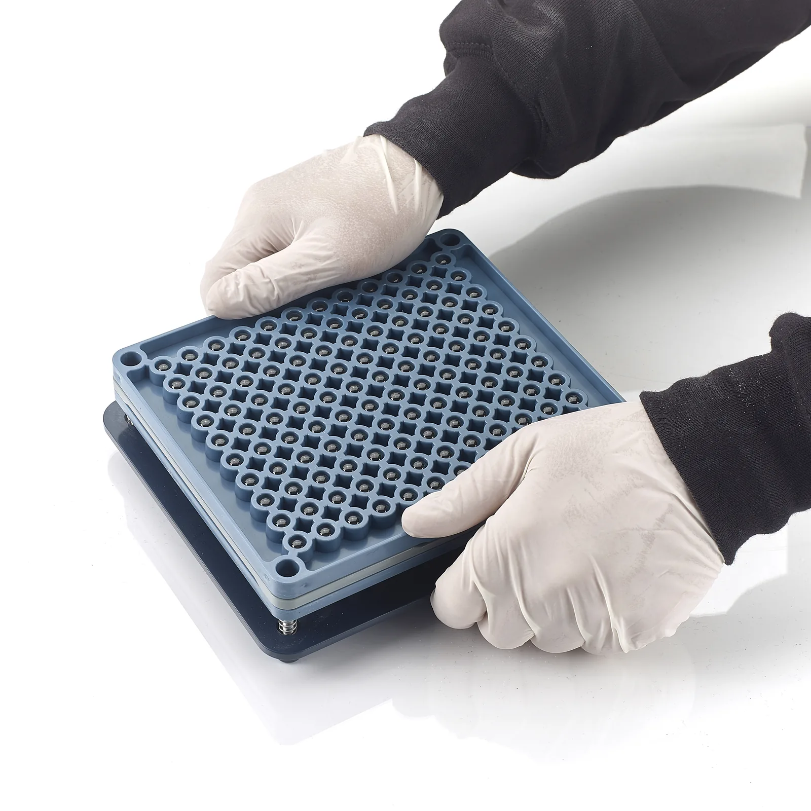 Gloved hands holding a closed blue manual capsule-filling plate.