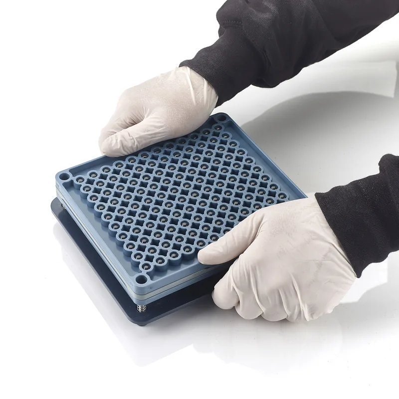 Gloved hands holding a closed blue manual capsule-filling plate.