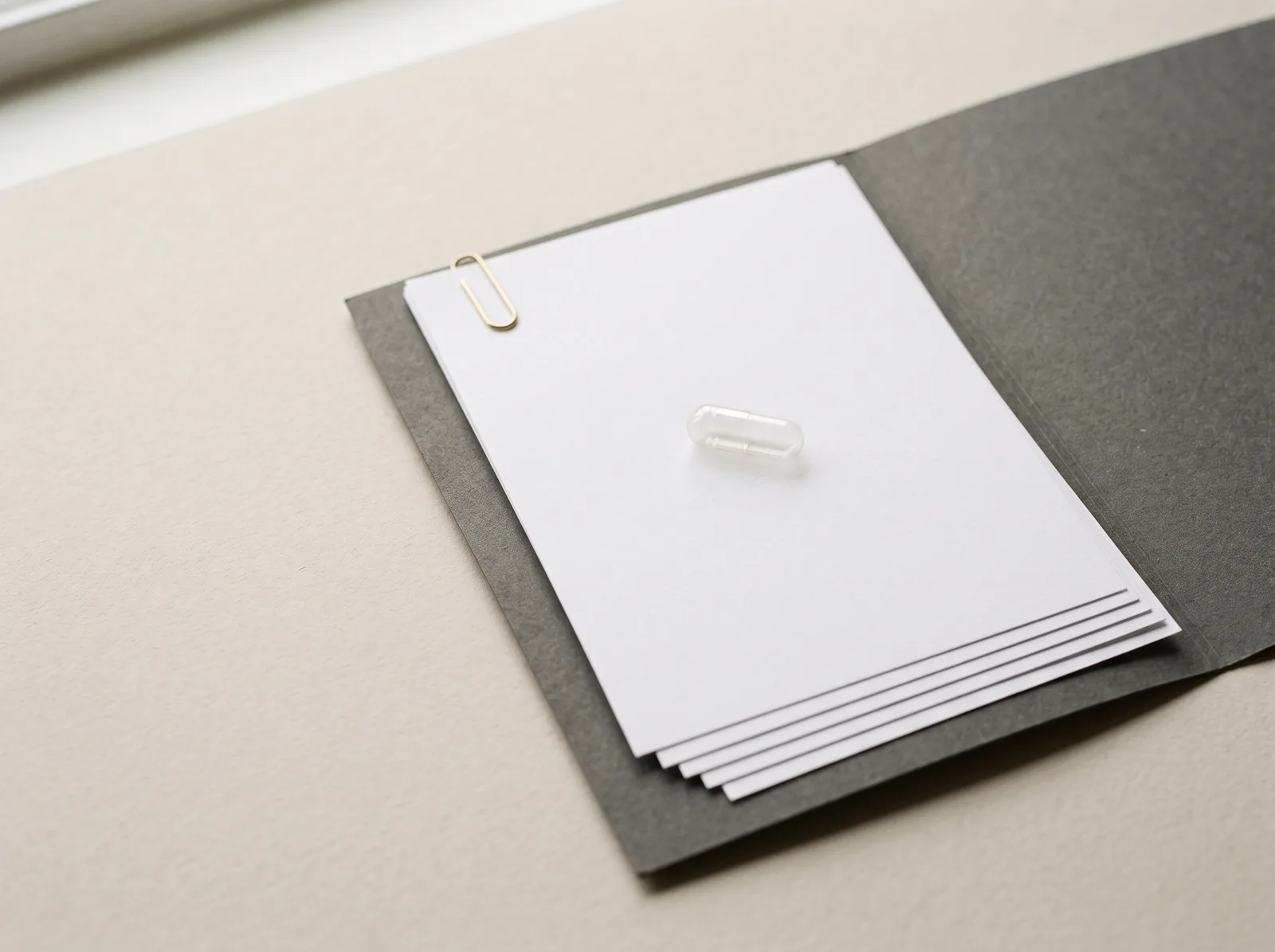 A clear empty capsule on a clipped stack of blank pages.