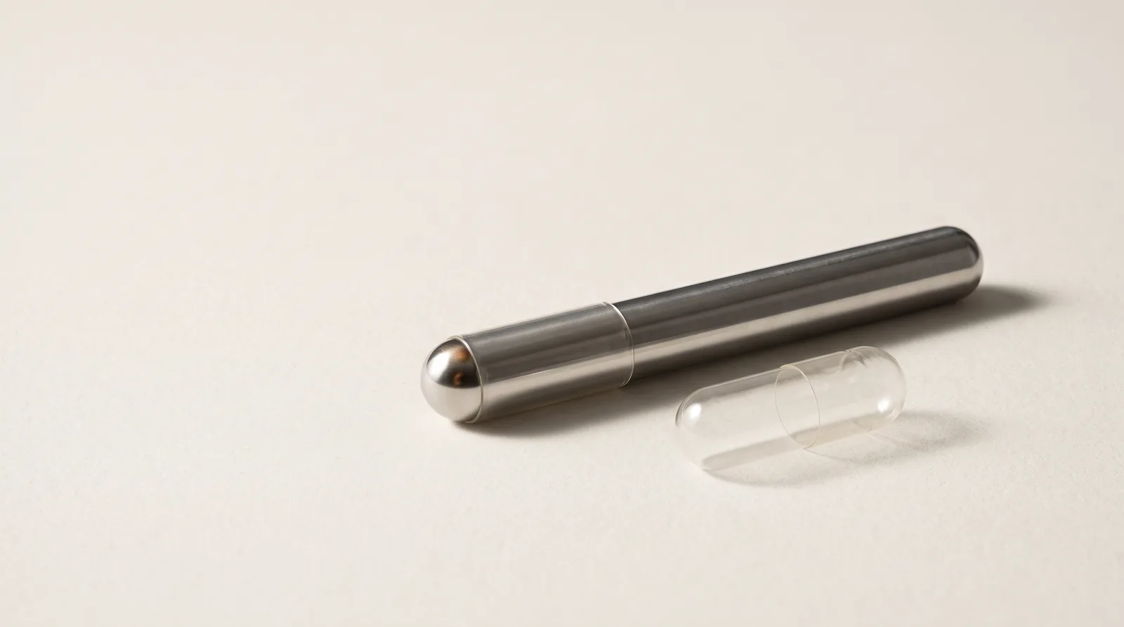 A polished steel dipping pin beside a clear empty capsule shell.