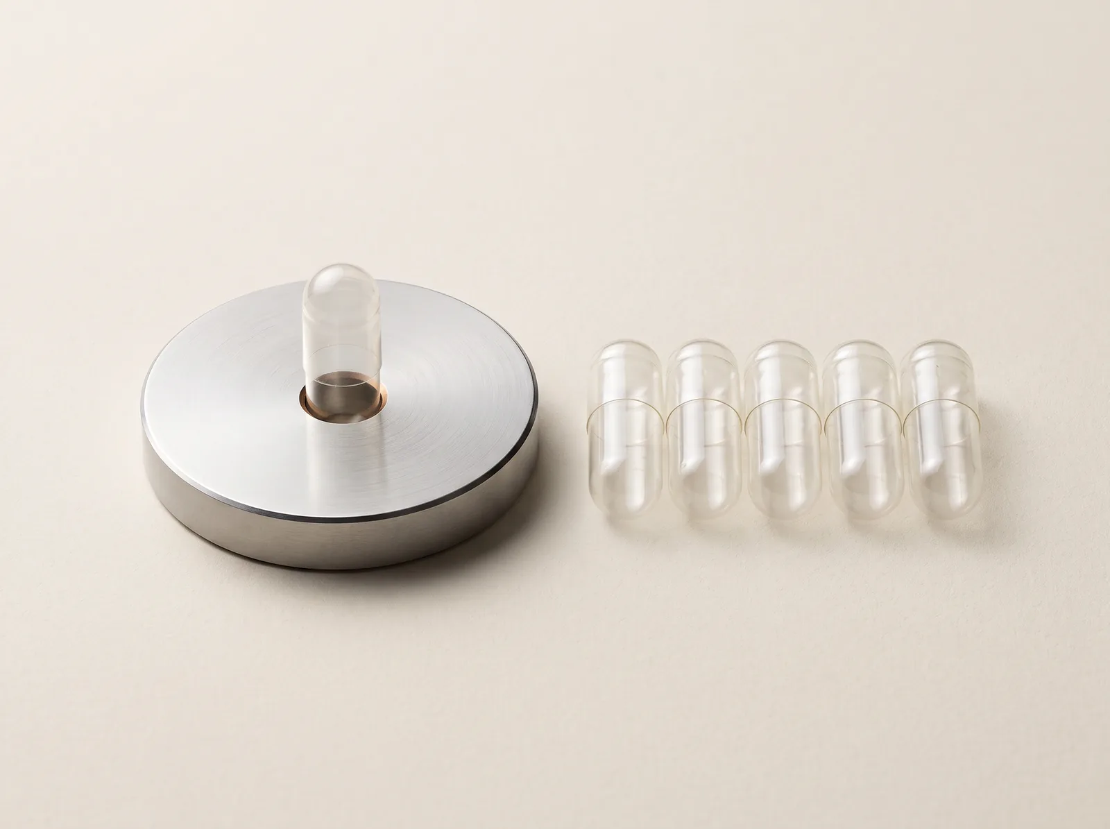 A capsule standing through a circular metal gauge beside several clear capsules.